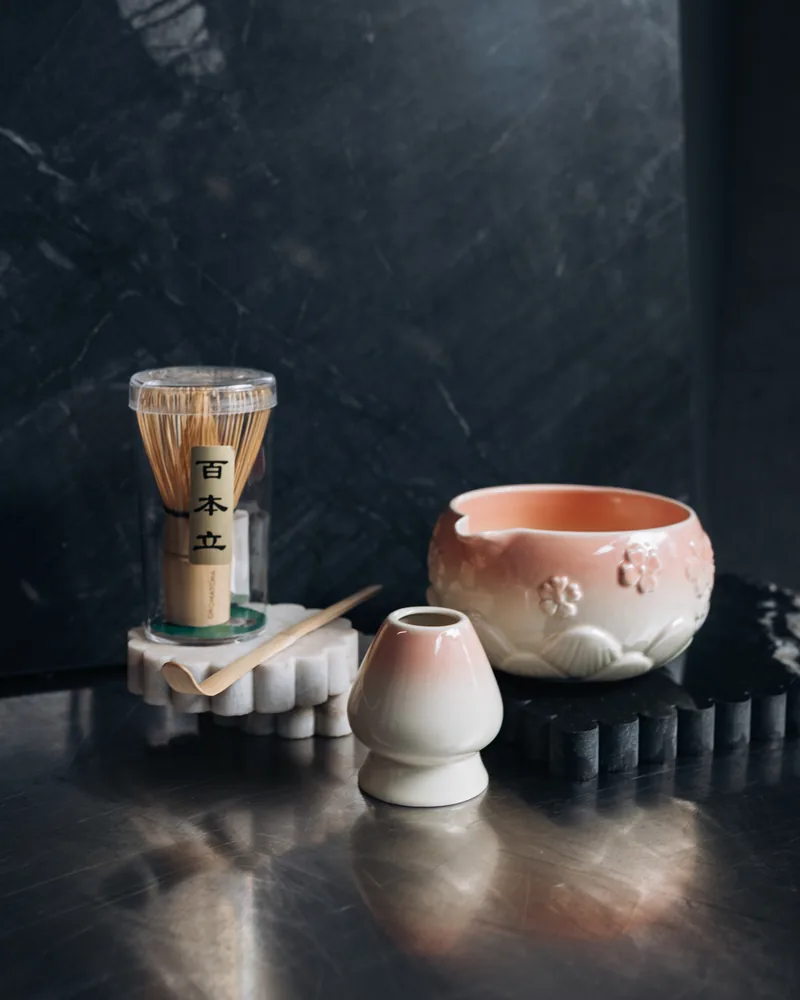 A pink ceramic matcha bowl with bamboo whisk and scoop
